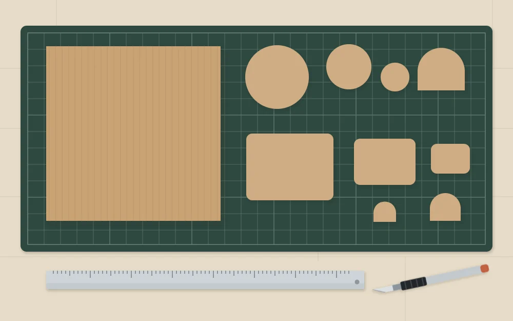 Cut cardboard shapes in three sizes beside a square base board, craft knife and metal ruler